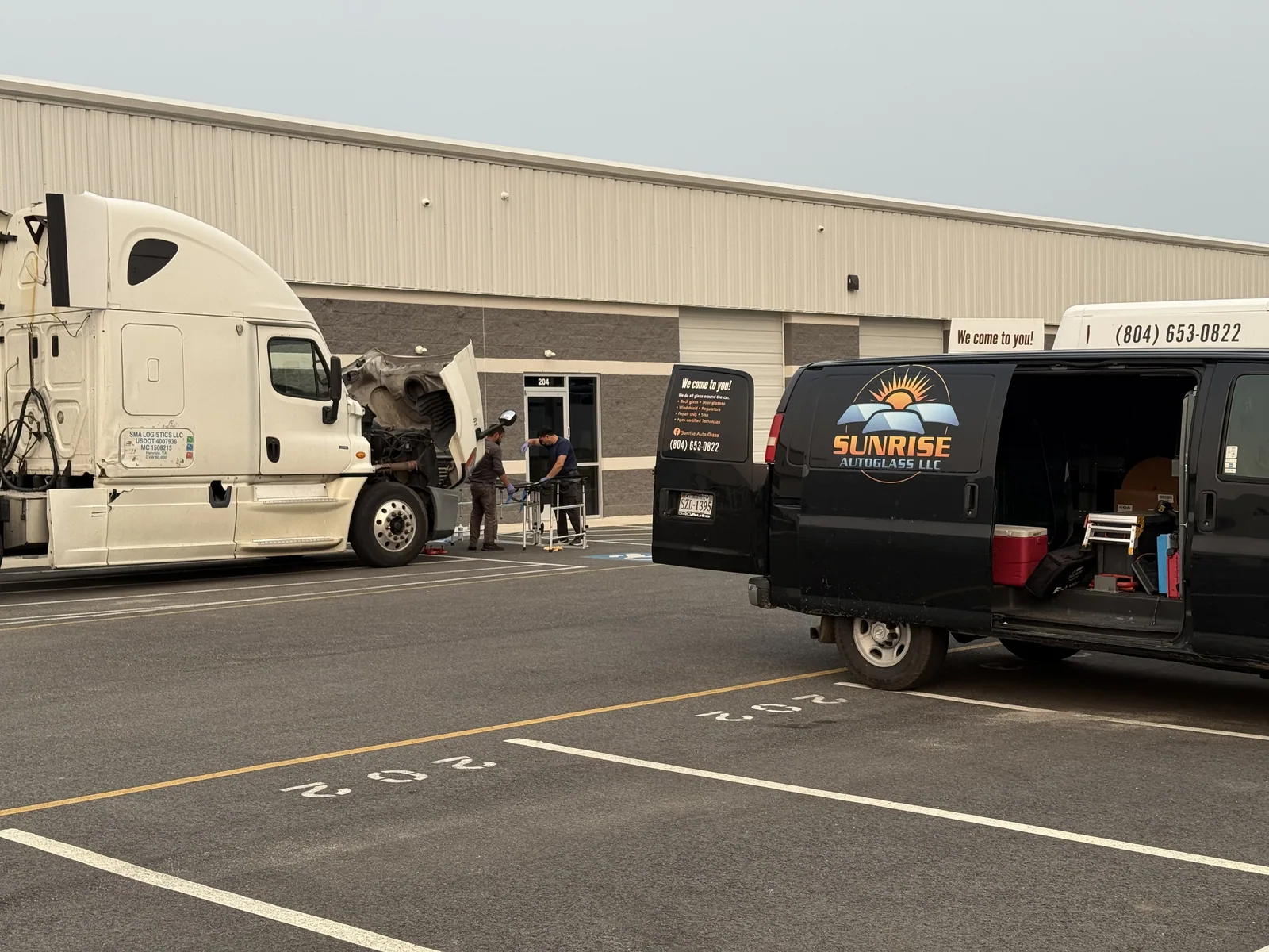 Technicians carrying a windshield to a semi truck outside the shop