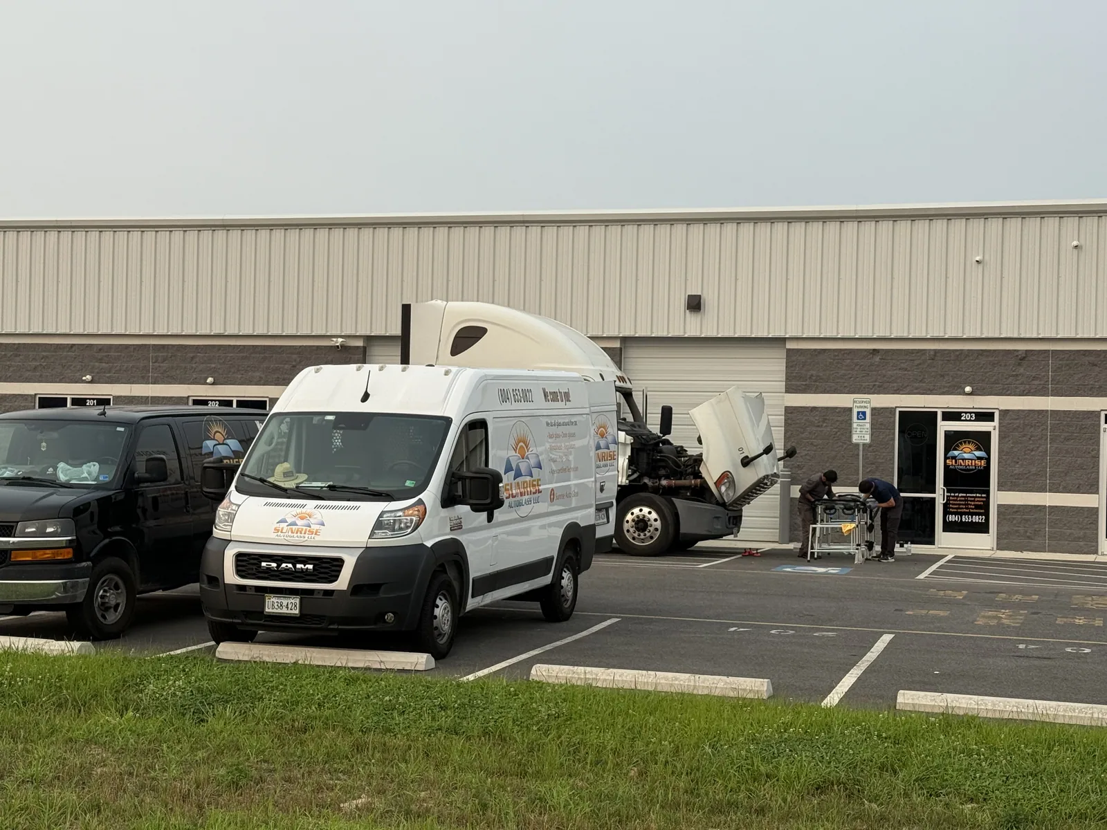 Sunrise AutoGlass vans parked outside the shop while technicians work on a semi truck